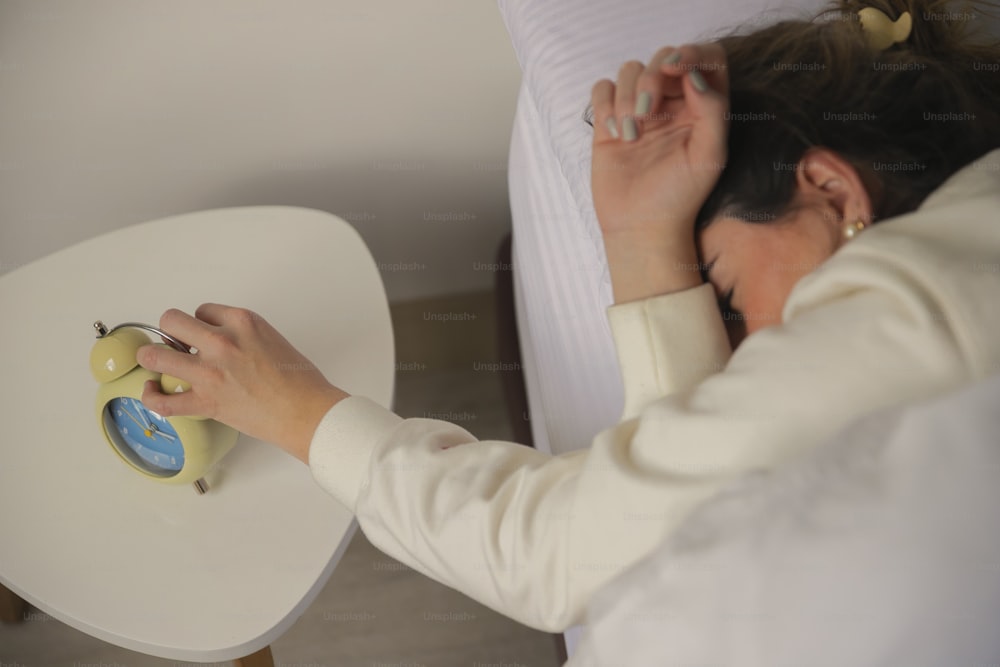 a woman laying in bed with a alarm clock on a table