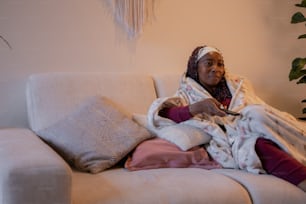 a woman sitting on a couch wrapped in blankets