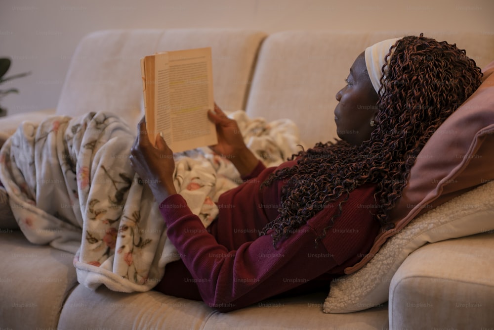 uma mulher sentada em um sofá lendo um livro