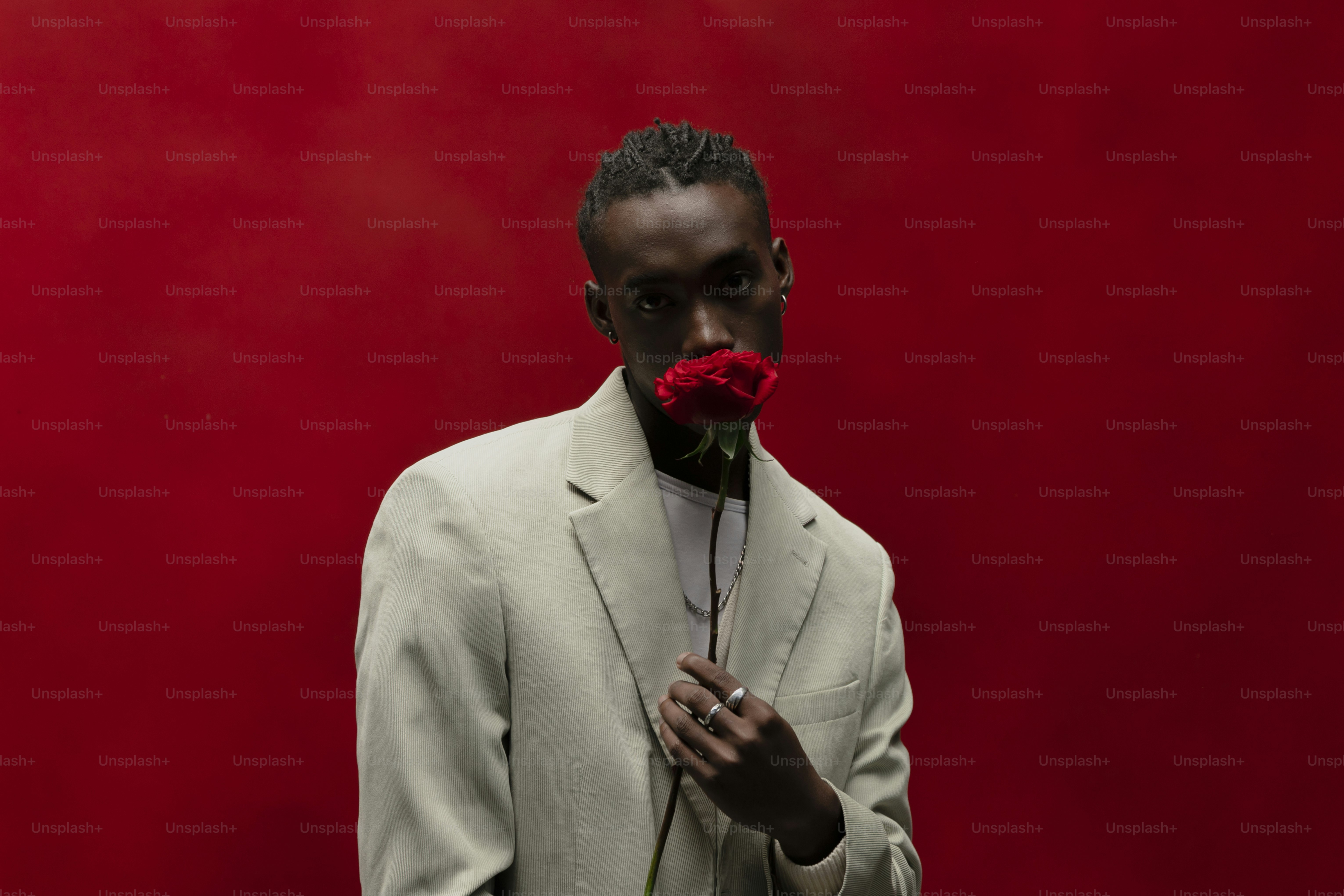 un homme en costume blanc avec une rose rouge dans la bouche