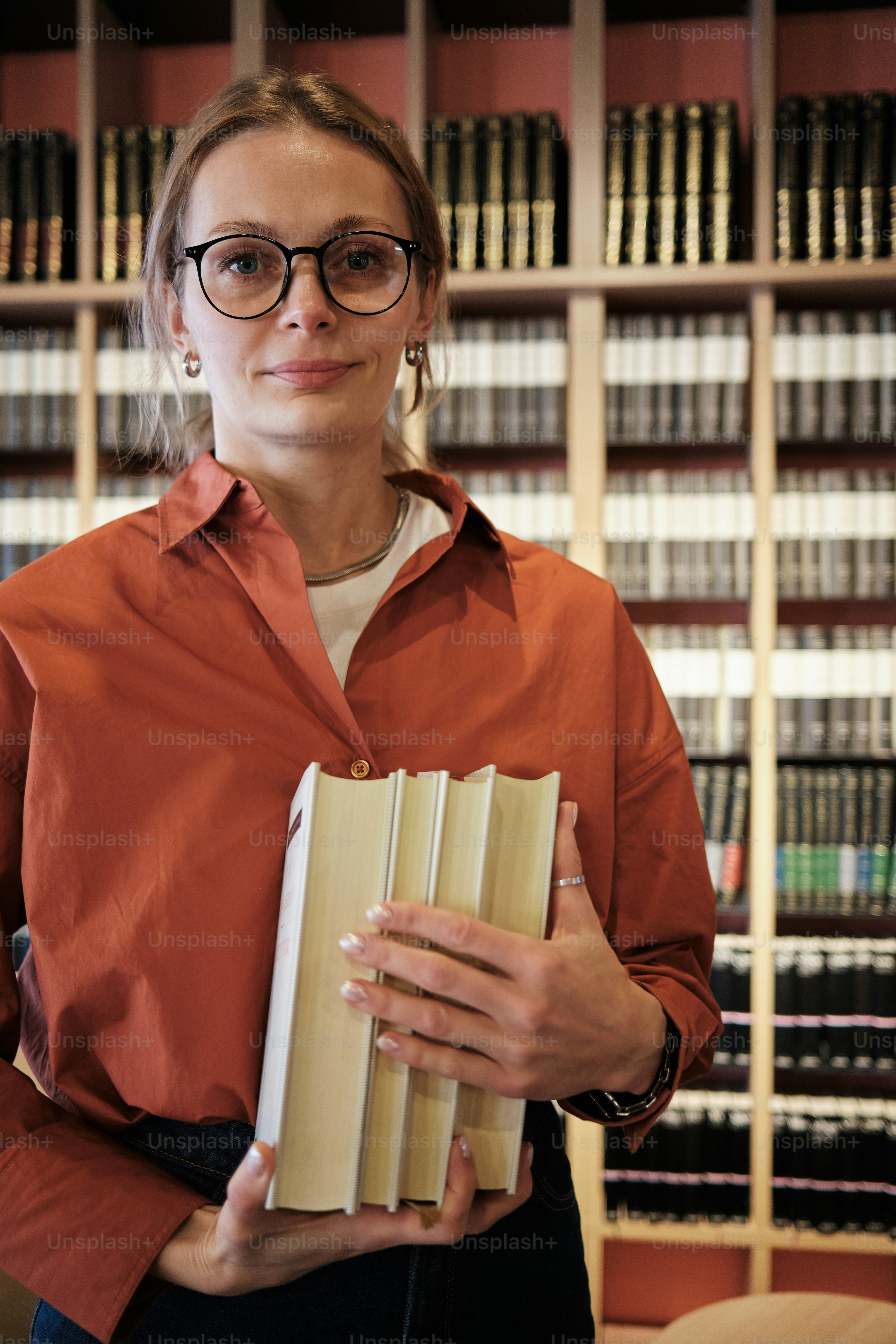 Woman in glasses holding books in a library