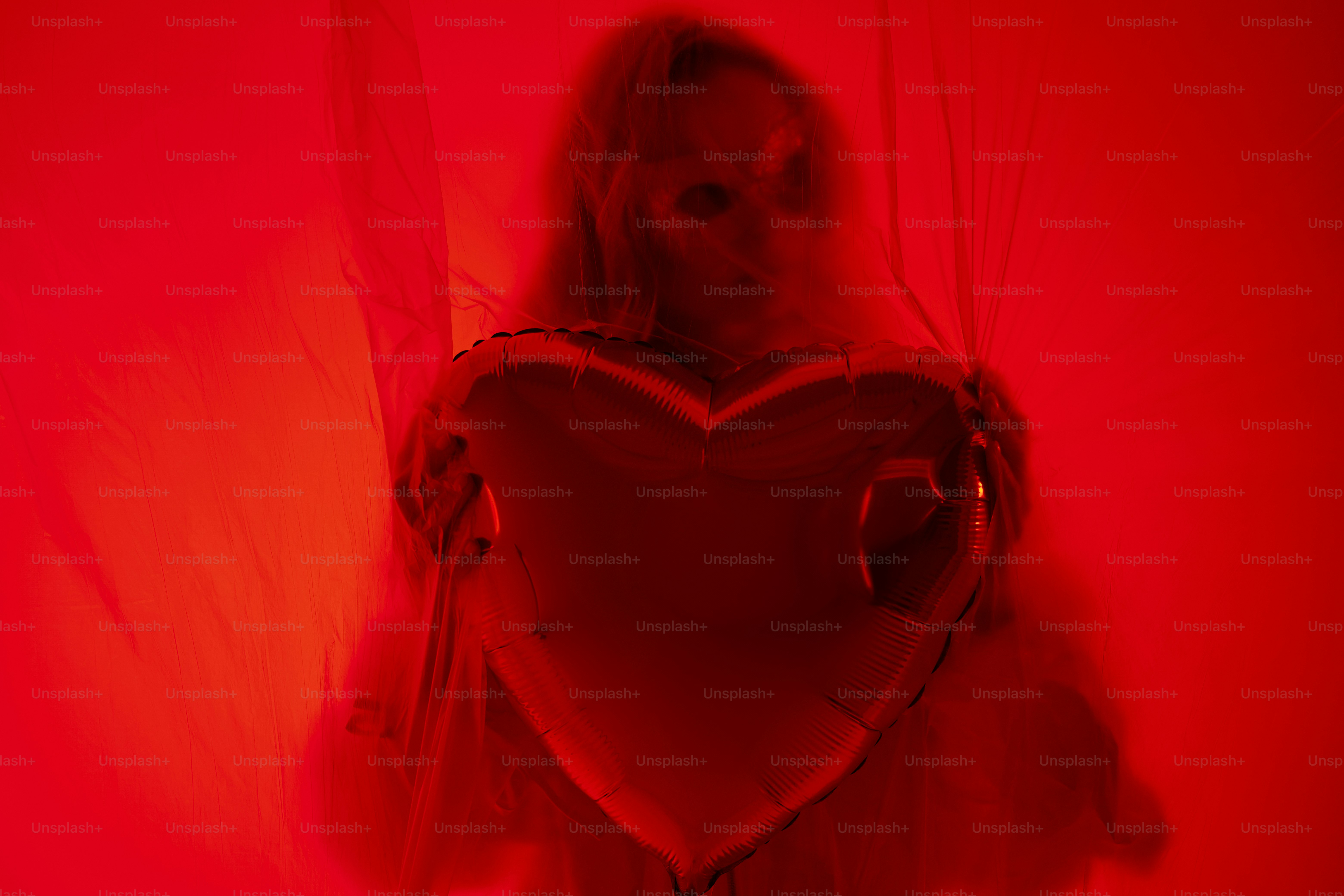 A person holding a red heart balloon in red light