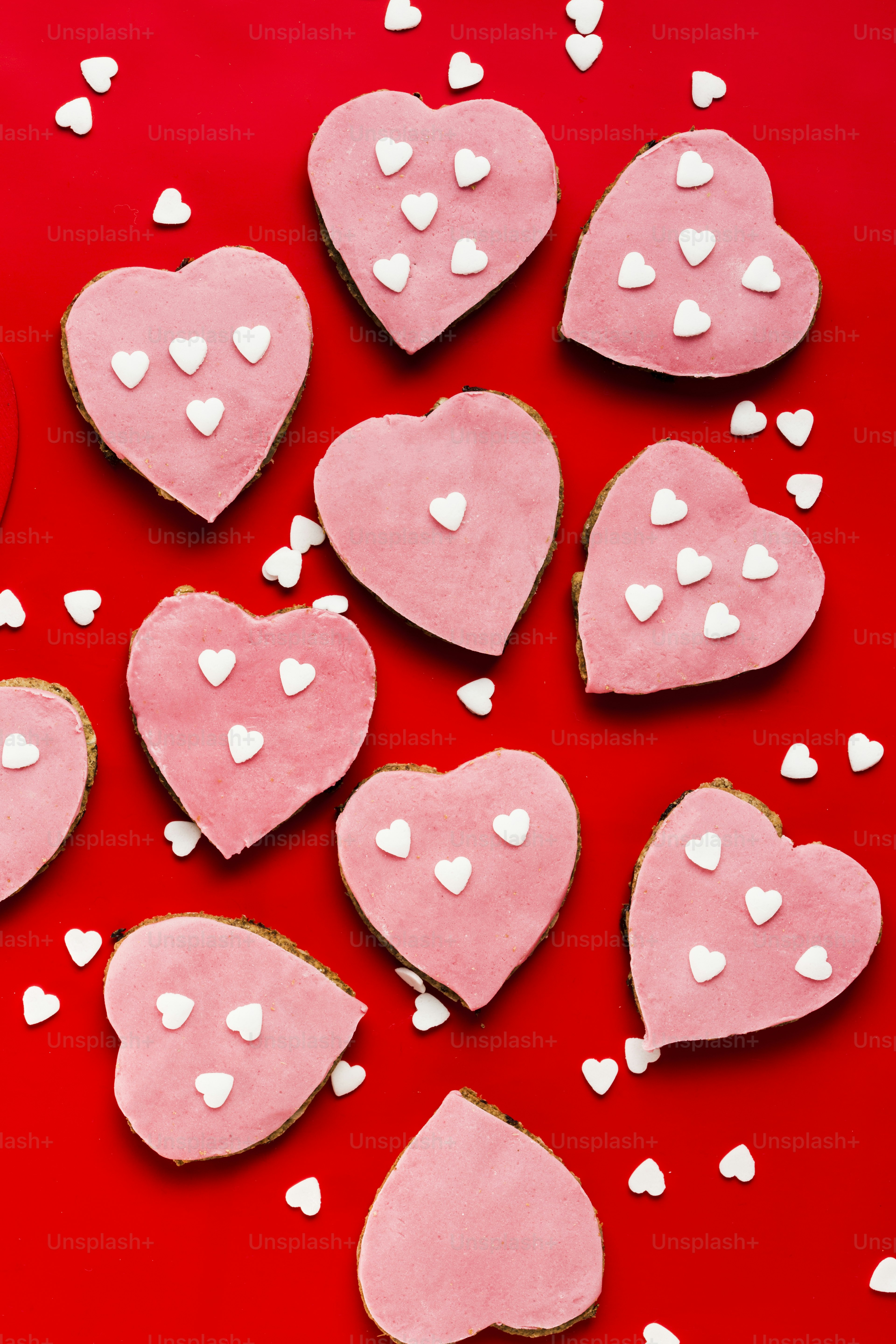 Rosa herzförmige Kekse mit weißer Glasur auf rotem Hintergrund