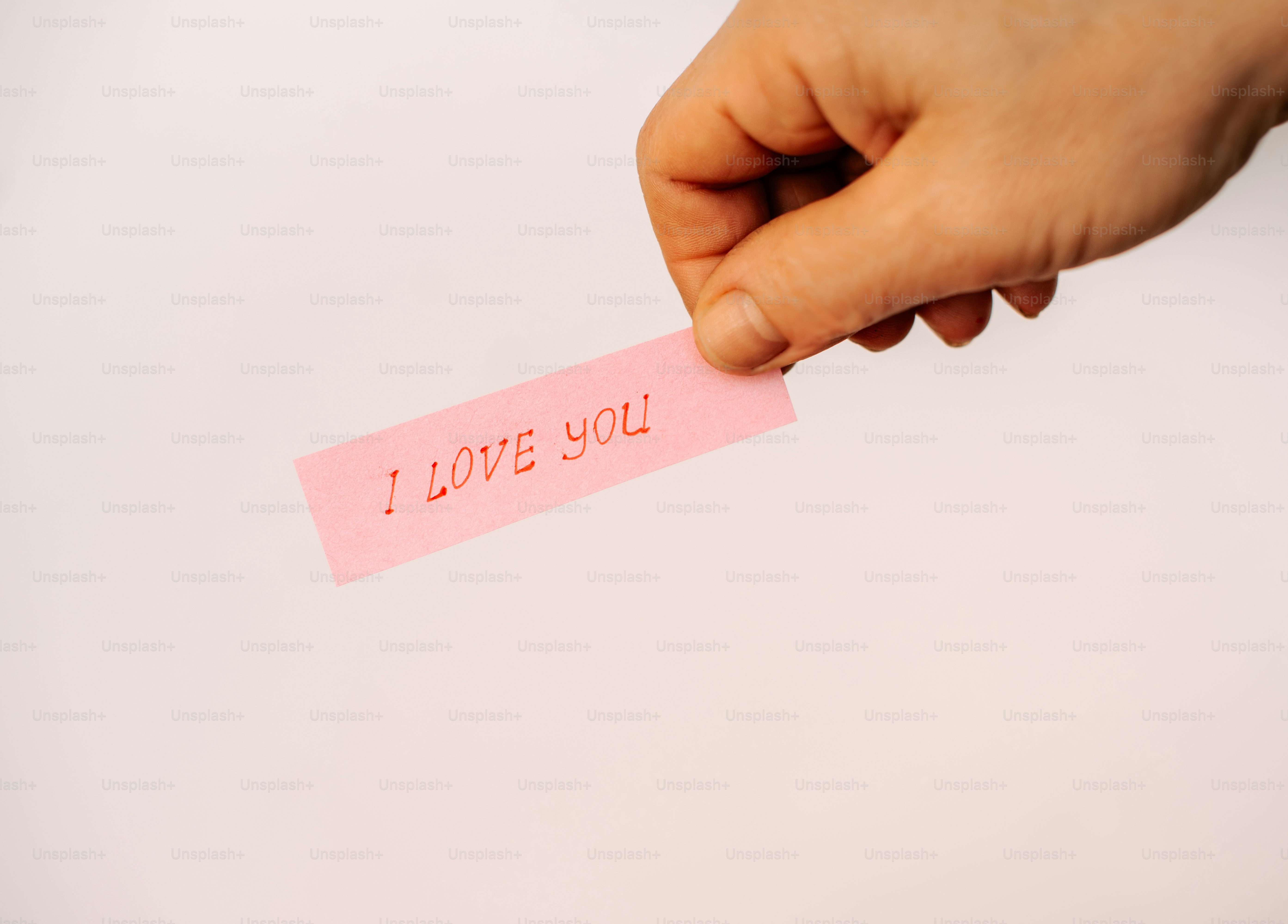 Hand holding a pink sticky note with "i love you".