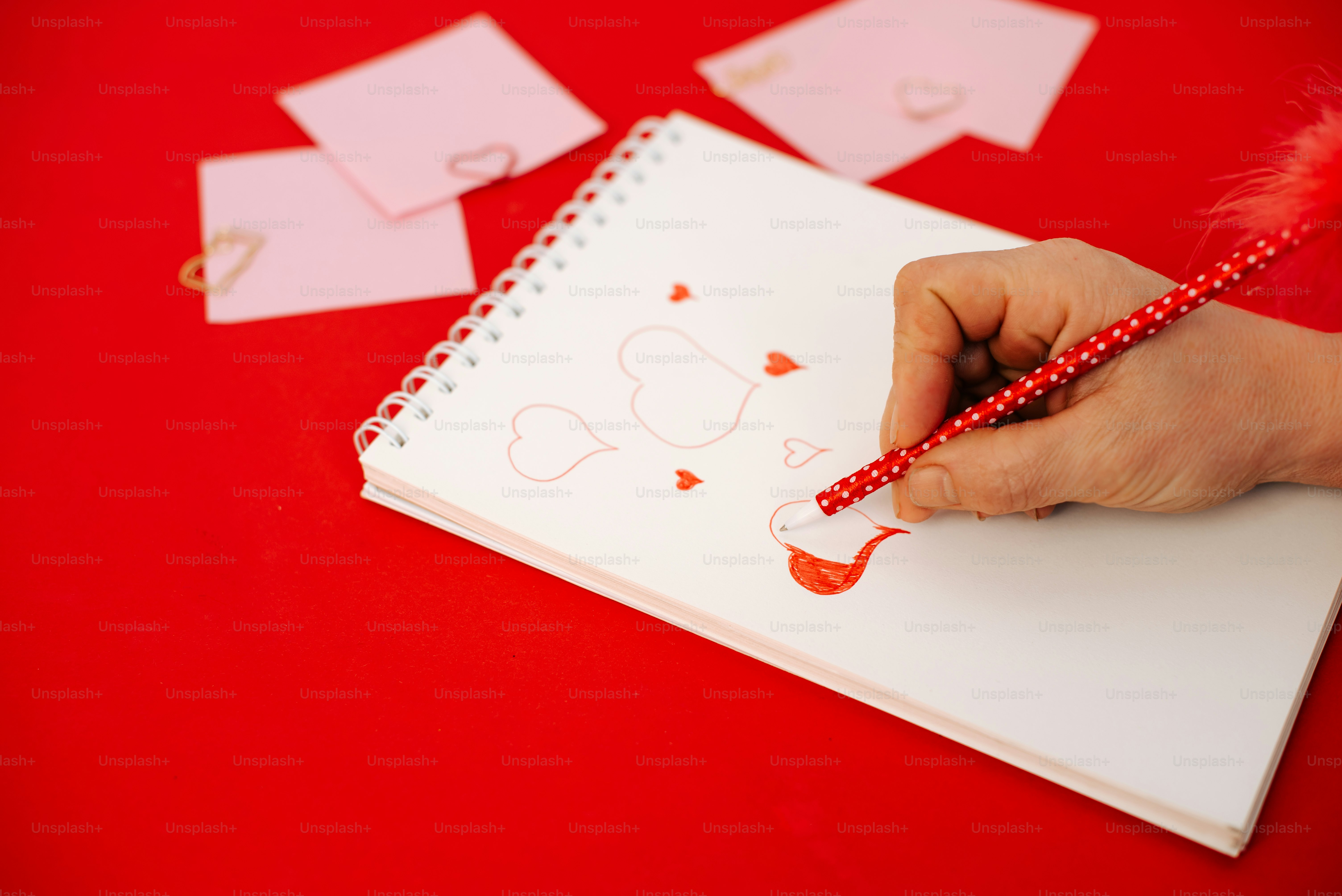 Hand drawing hearts on a notebook with a feather pen.