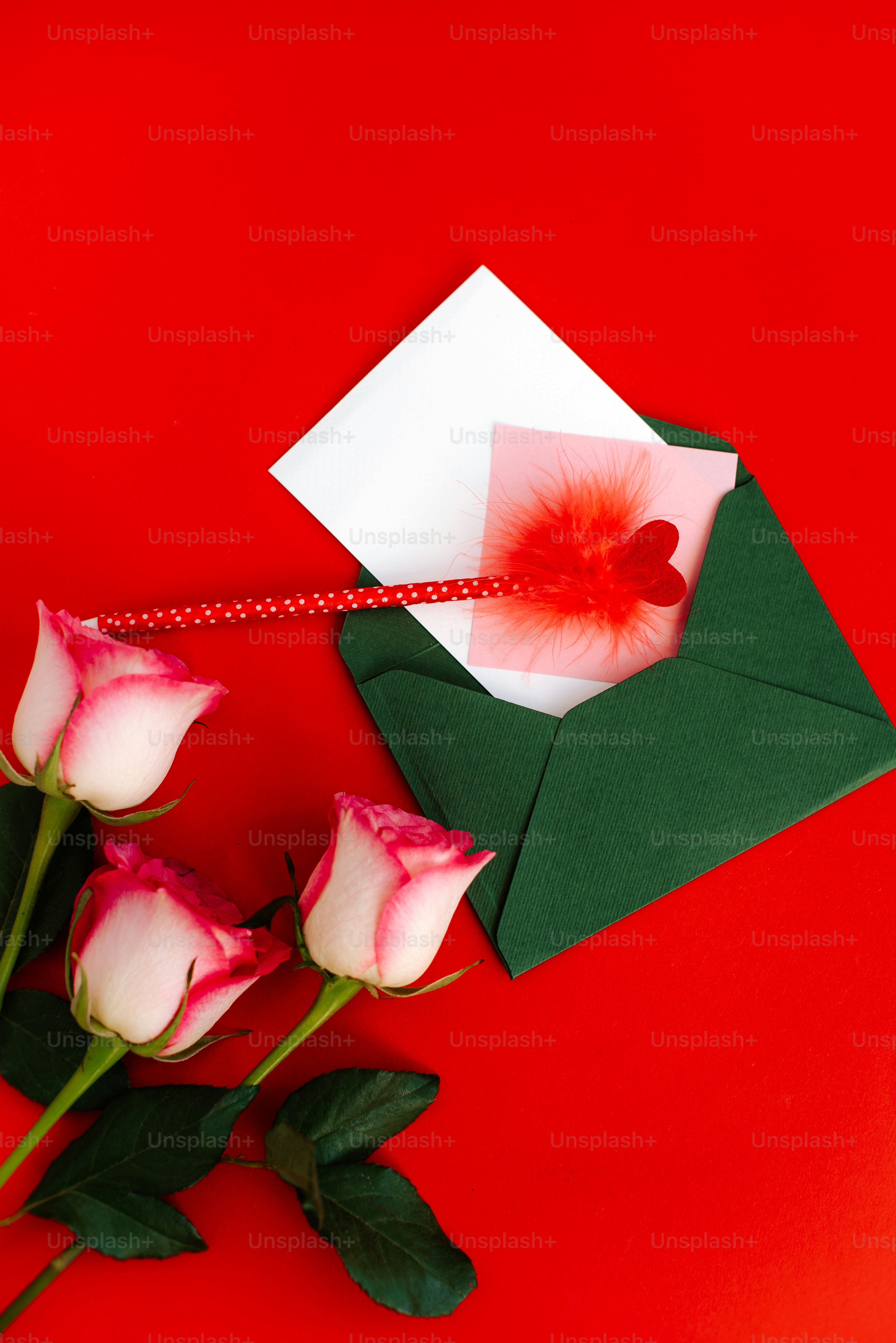 Three pink-tipped roses and an open envelope on red