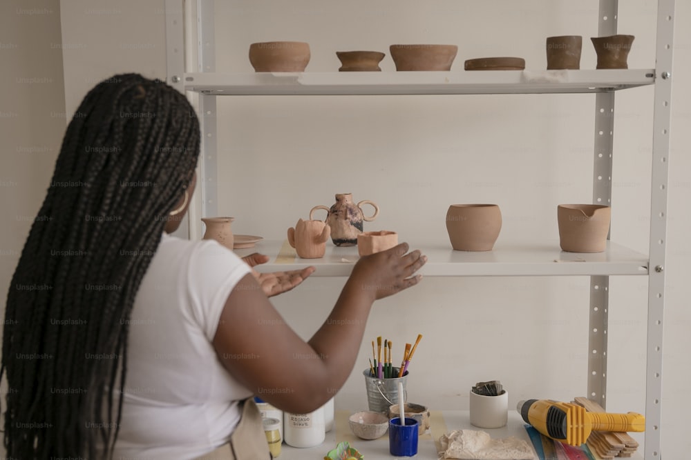 a woman standing in front of a shelf filled with pottery
