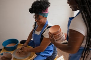 a woman in a blue apron and a girl in a white shirt are making clay