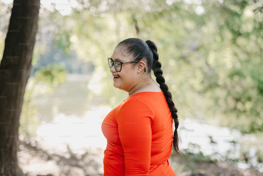 a woman in an orange shirt is standing near a tree