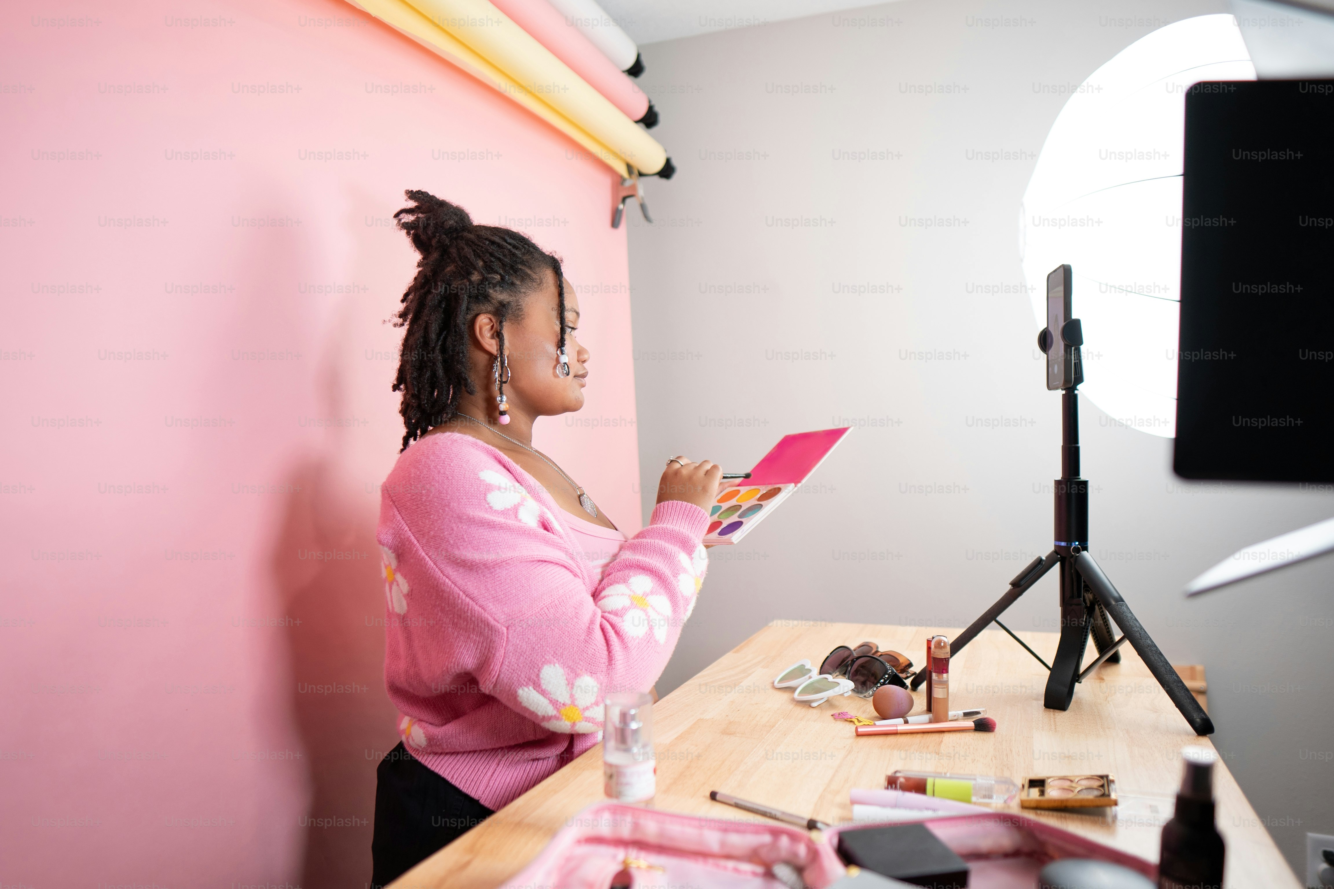 a woman sitting at a desk in front of a pink wall