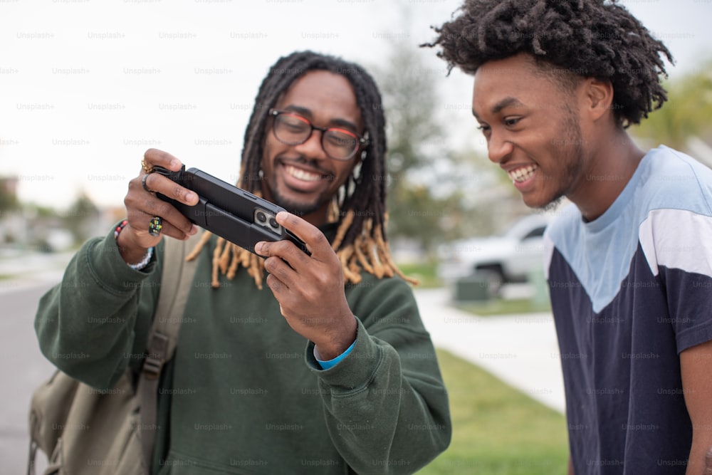 two young men standing next to each other looking at a cell phone