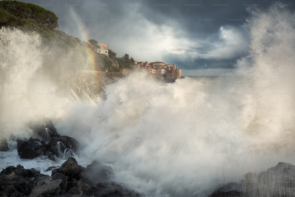a large wave crashing into the shore with houses in the background