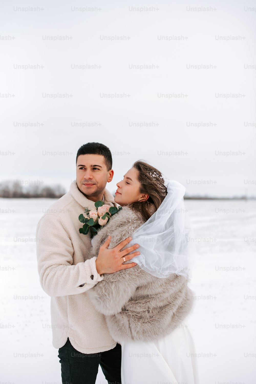a bride and groom embracing in the snow