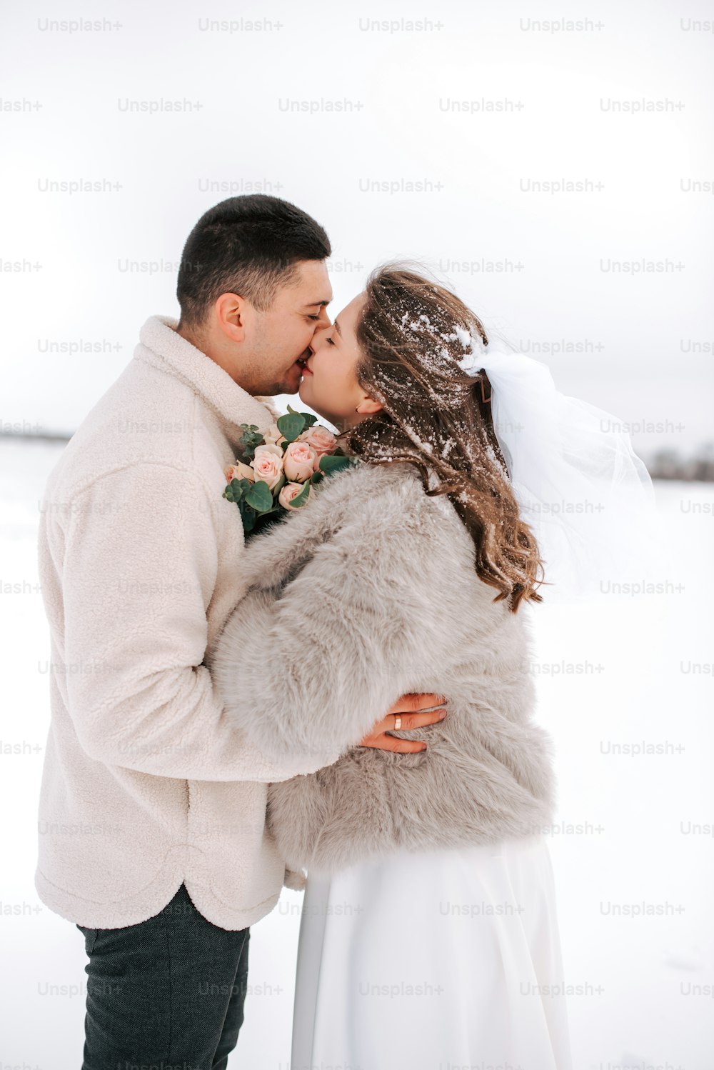 a bride and groom kissing in the snow