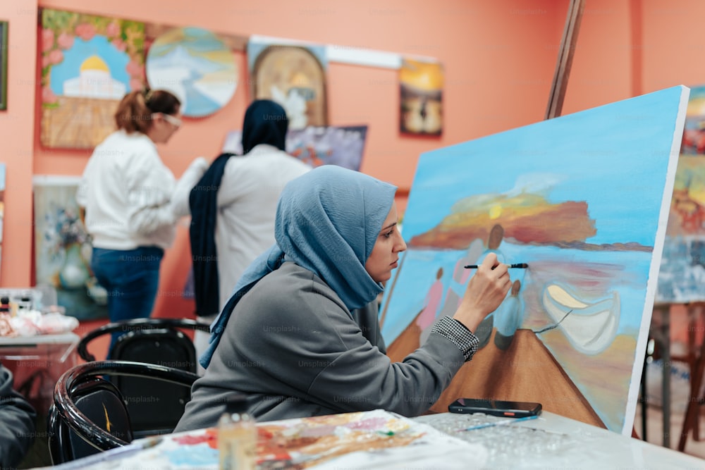une femme dans un hijab peignant une image sur une toile
