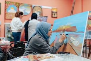 ヒジャブをかぶった女性がキャンバスに絵を描く