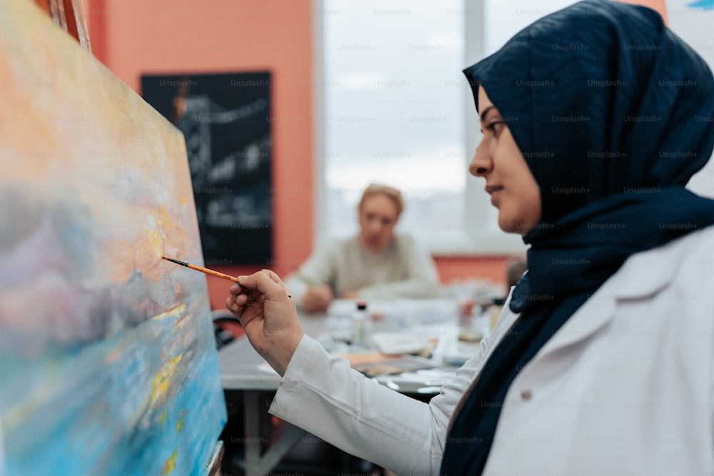 a woman in a hijab painting on a canvas