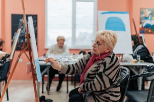 an older woman sitting in a chair in front of a easel