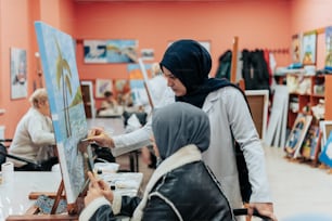 ヒジャブをかぶった女性がイーゼルに絵を描いている