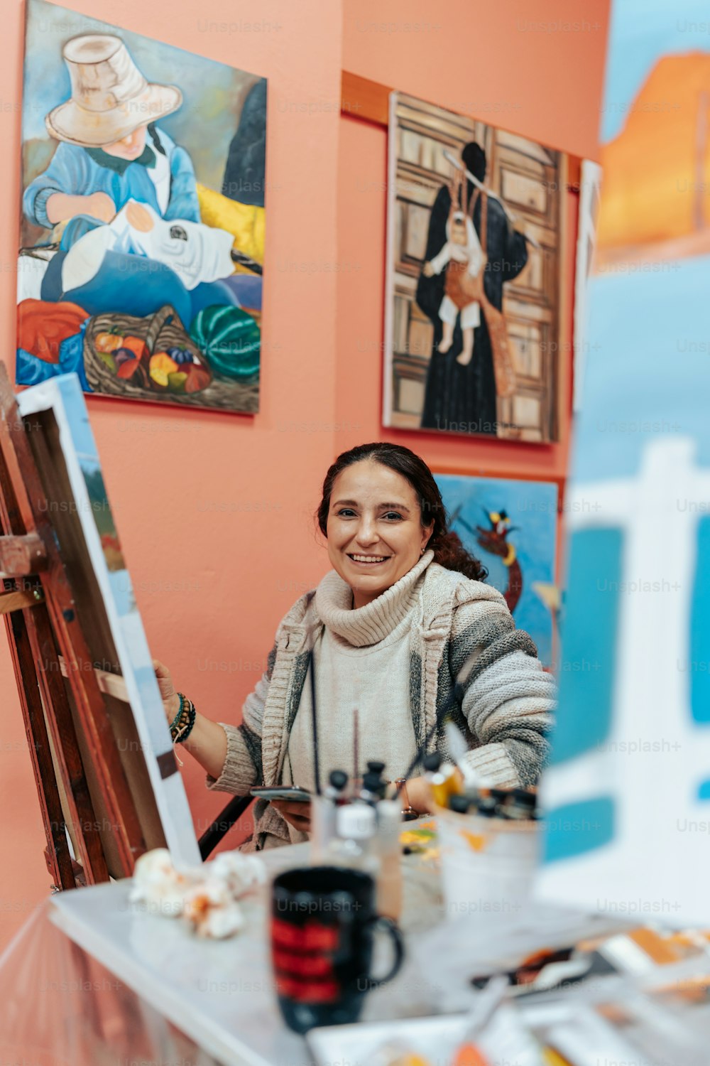 a woman sitting in front of a painting on a easel