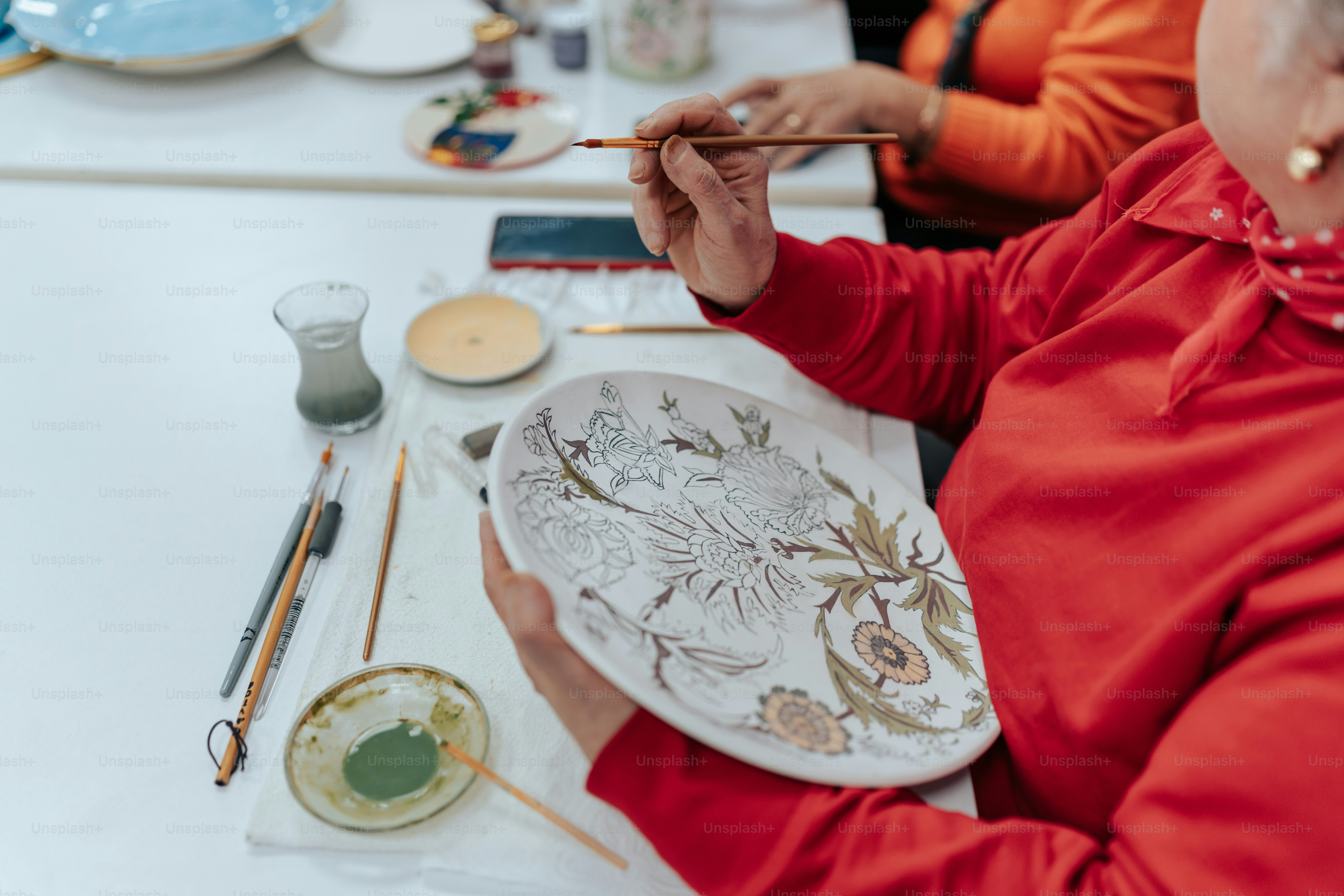 a woman in a red shirt is painting a picture on a plate