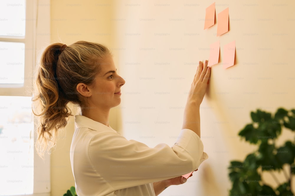 Uma mulher de camisa branca está colocando notas adesivas em uma parede