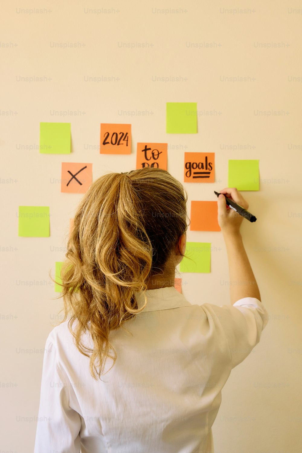 a woman writing on a wall with sticky notes