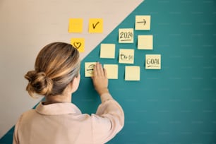 a woman writing on a wall with sticky notes