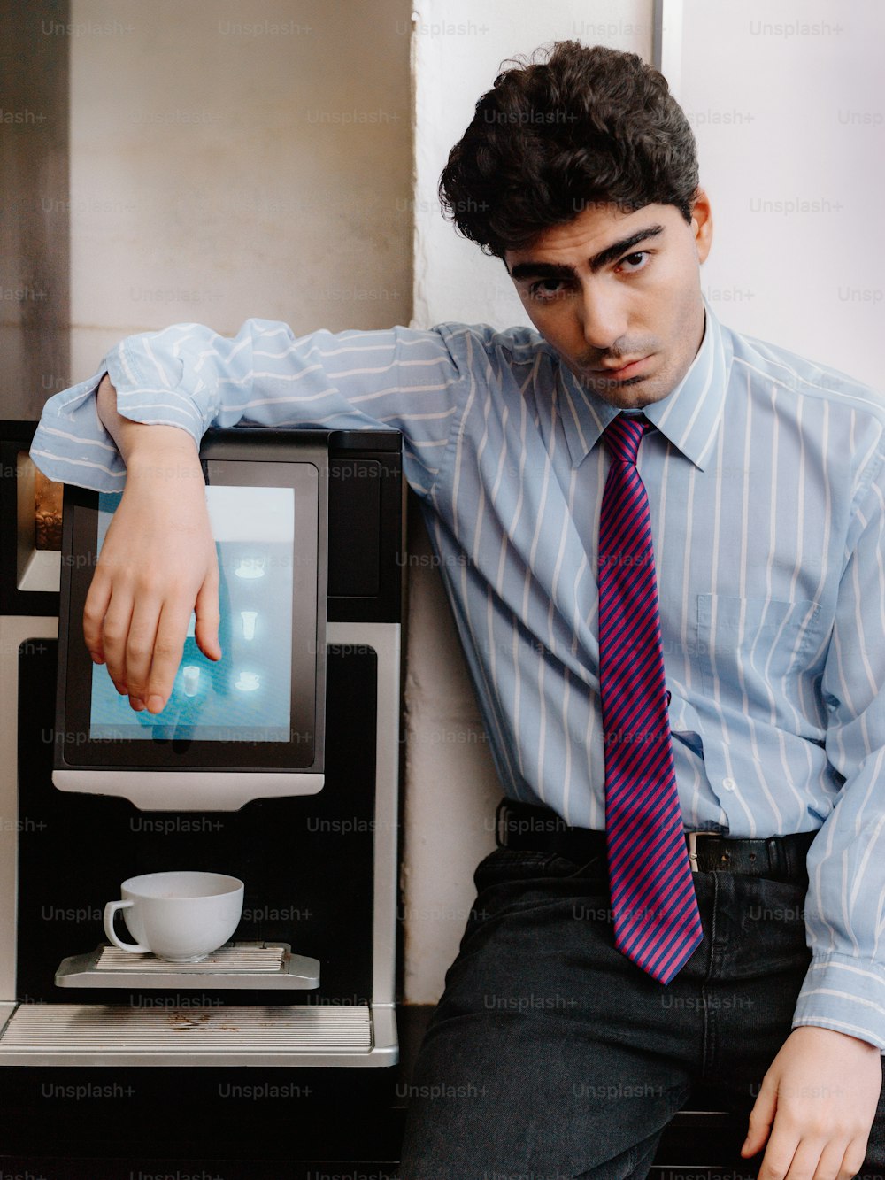 a man in a tie leaning against a coffee machine