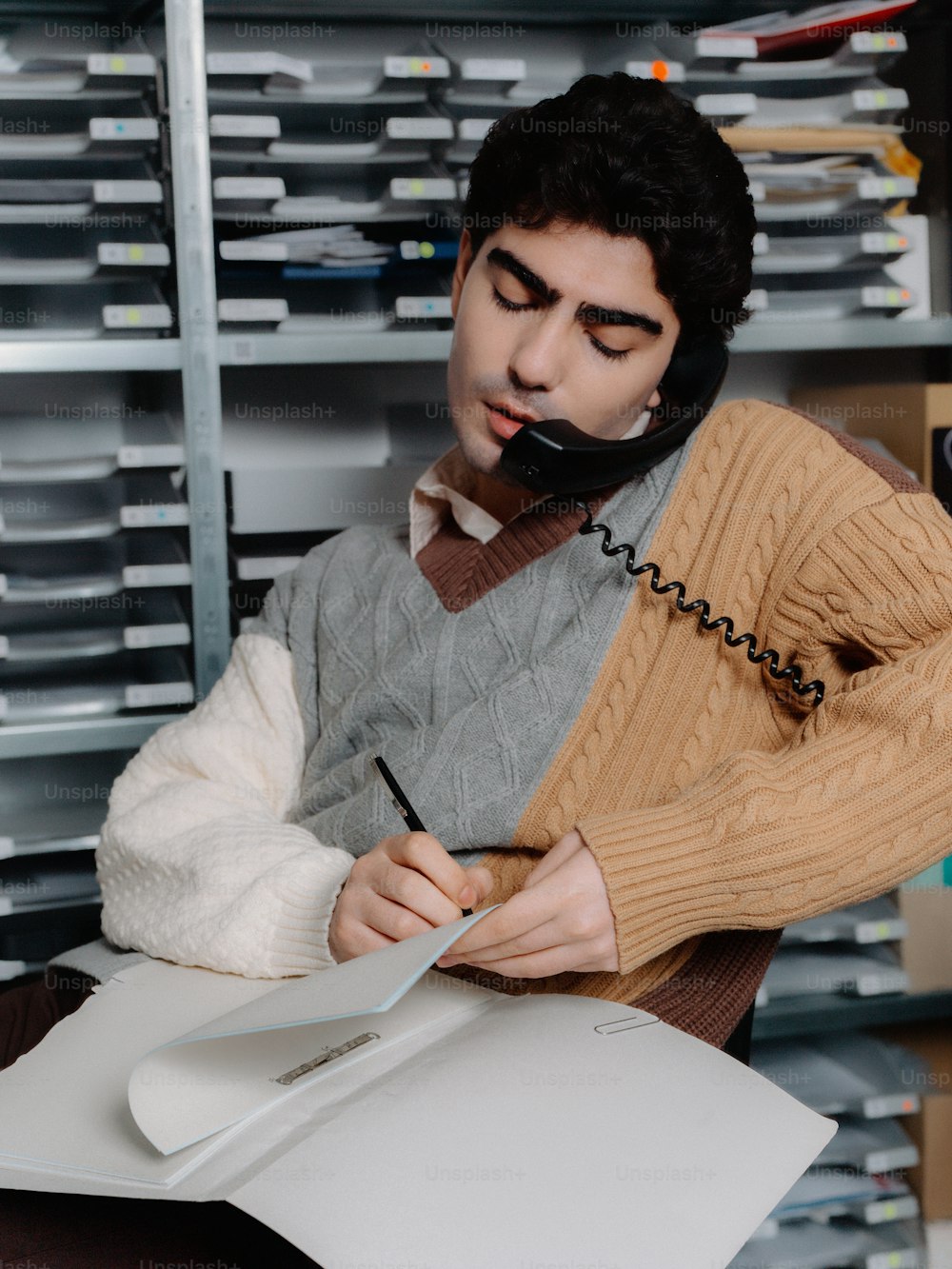 a man in a sweater holding a clipboard and a telephone