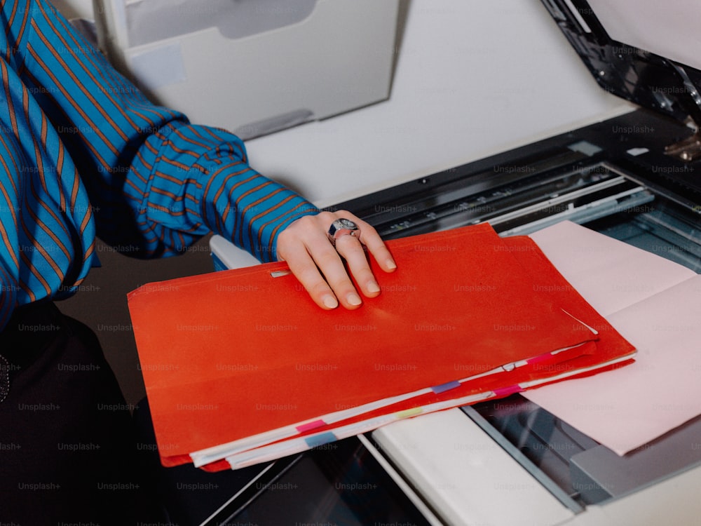 a person holding a binder in front of a printer
