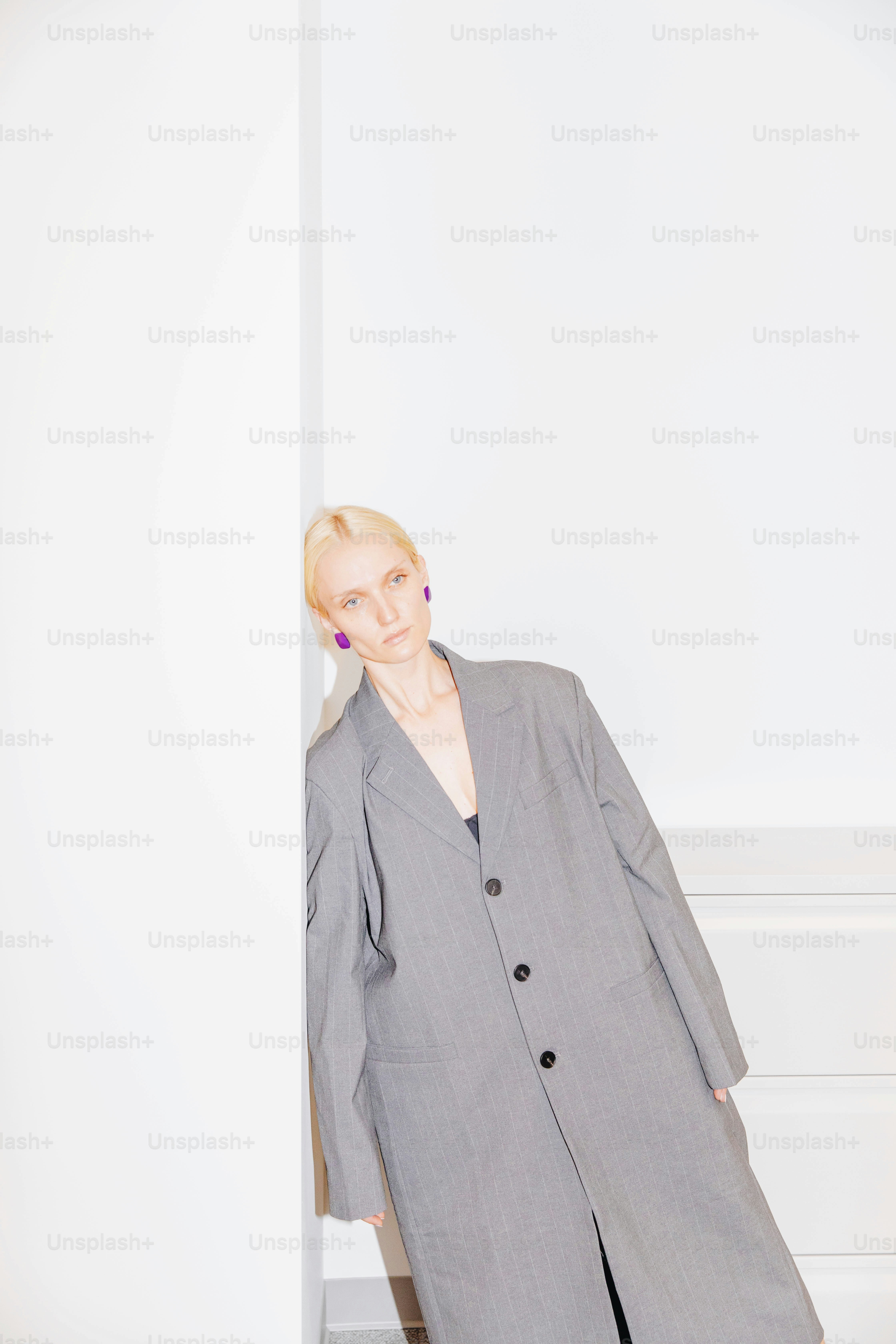 a woman in a gray suit leaning against a wall