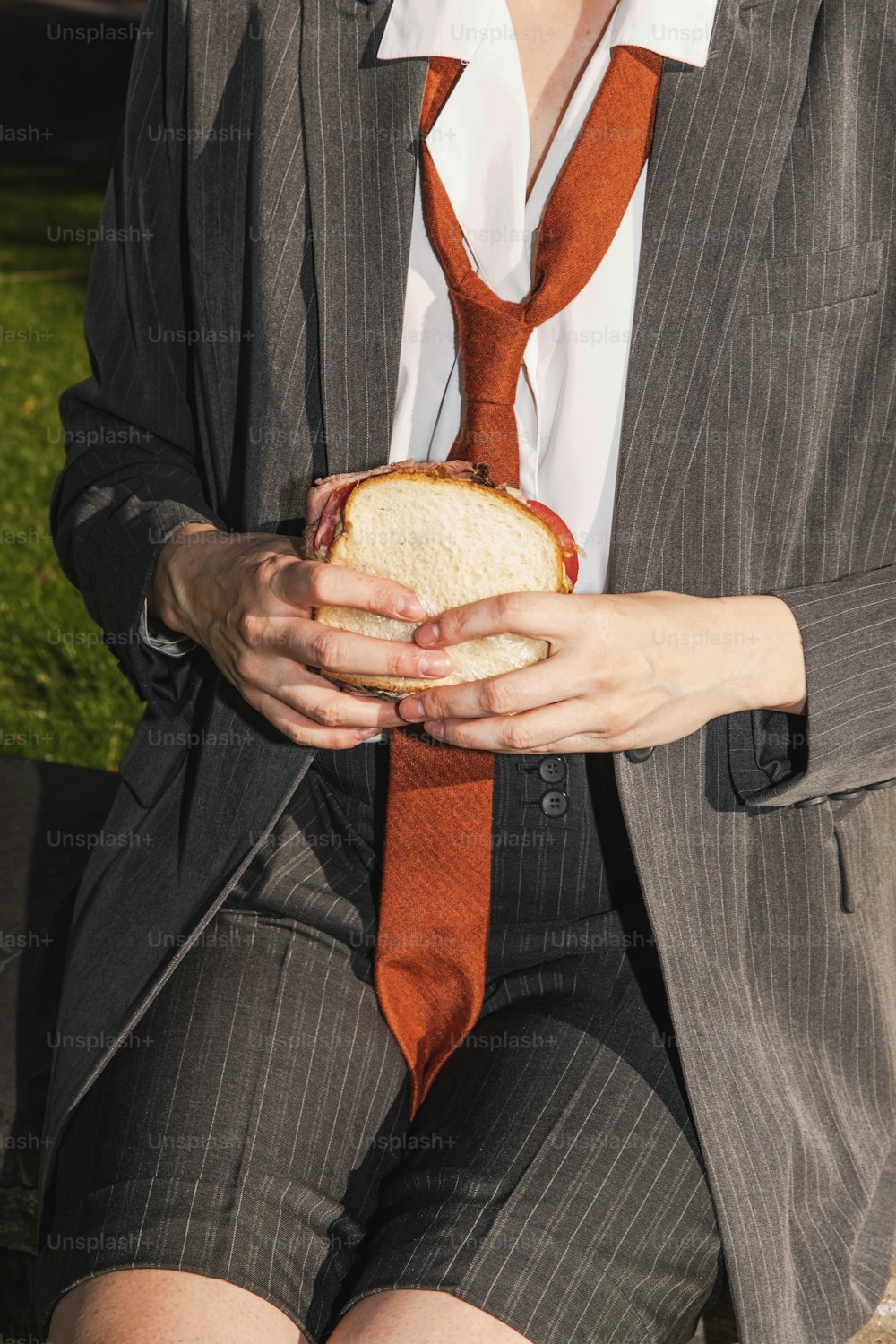 eine Frau in Anzug und Krawatte hält ein Sandwich in der Hand