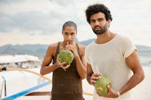 a man and a woman standing on a beach holding fruit