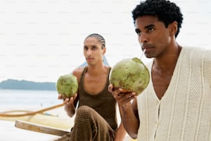 a man and a woman sitting on a beach holding coconuts