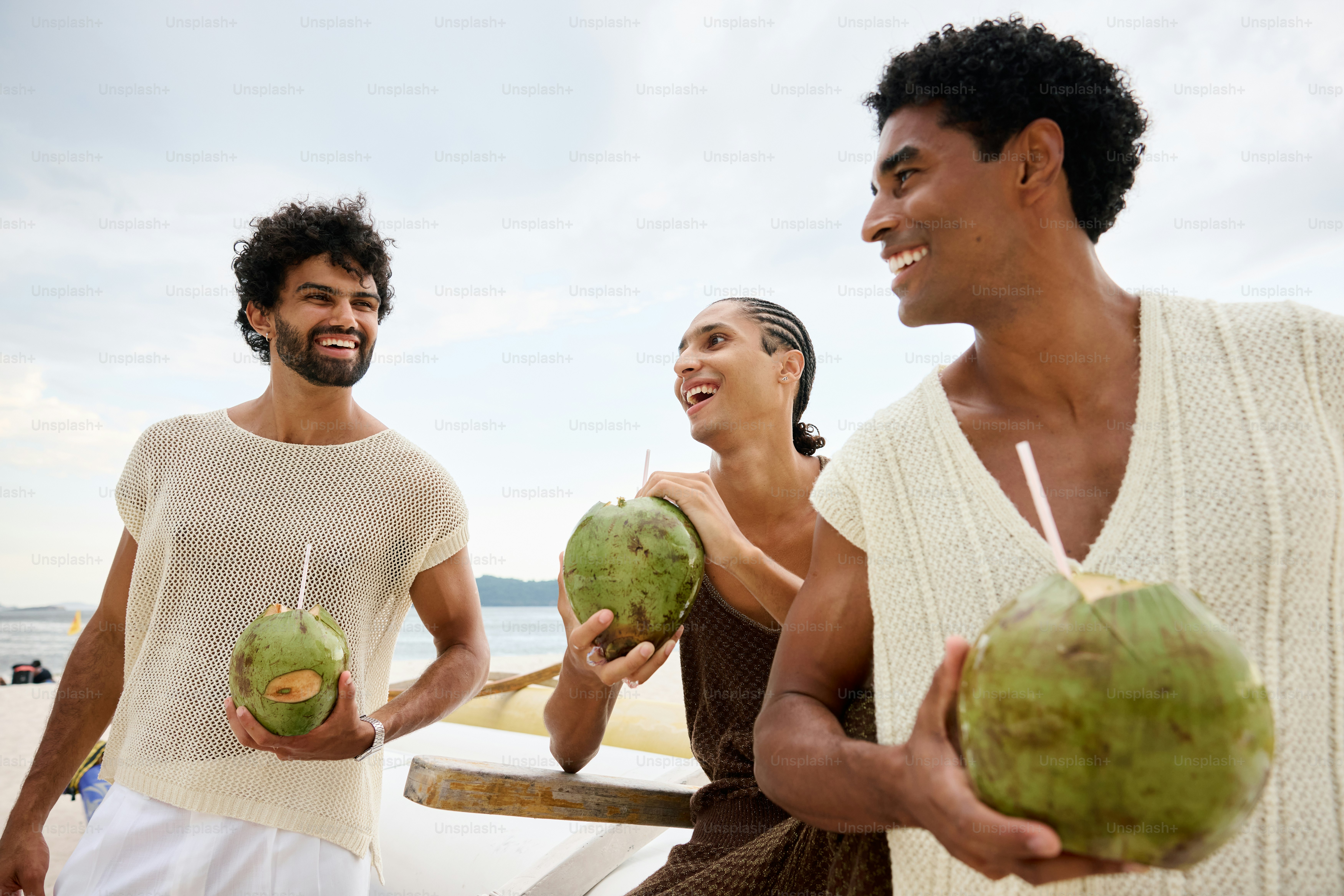 two men and a woman holding coconuts on a beach