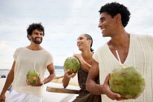 due uomini e una donna che tengono noci di cocco su una spiaggia