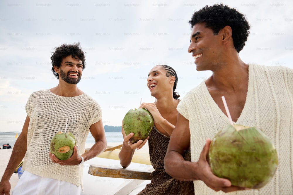 two men and a woman holding coconuts on a beach