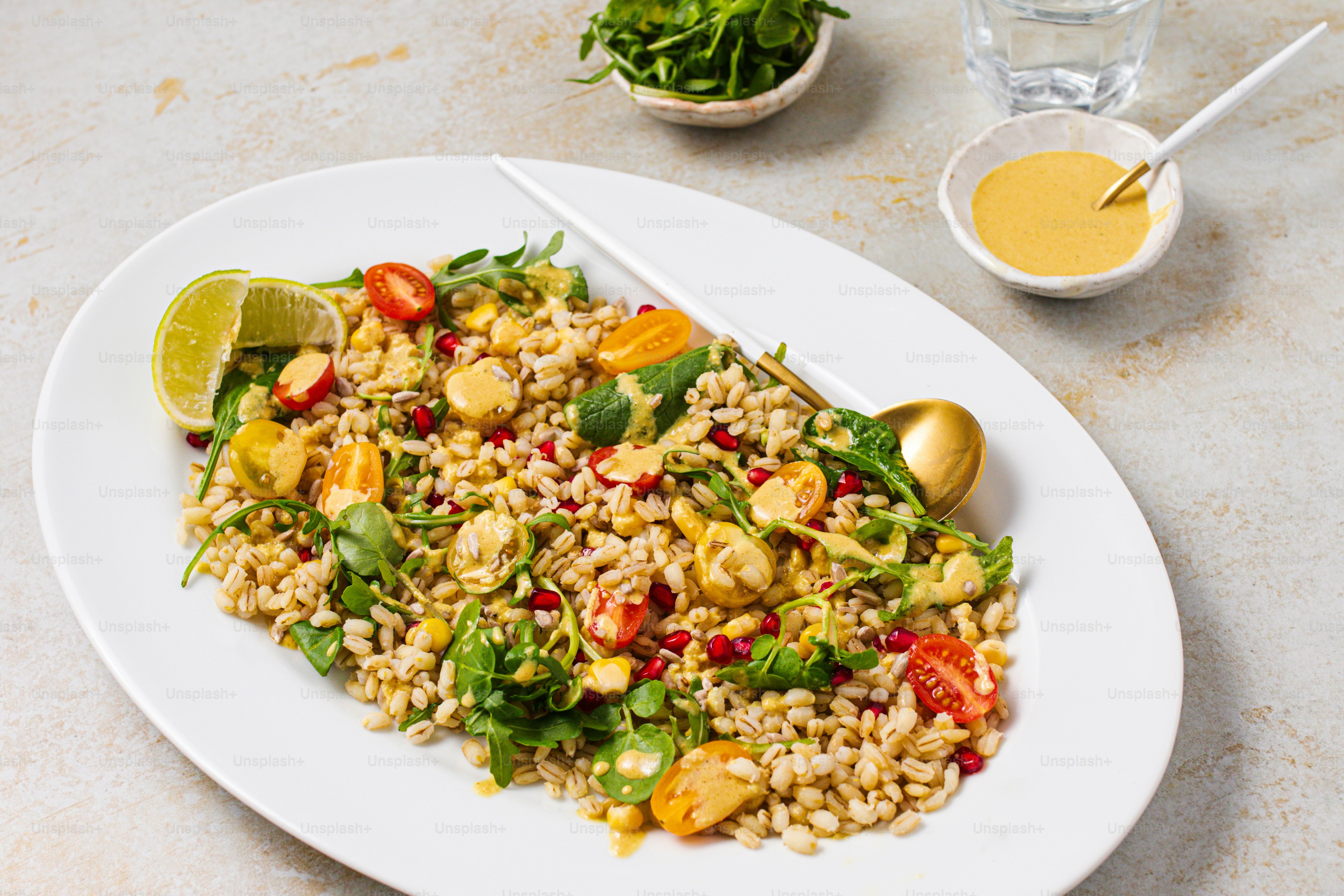 a white plate topped with a salad next to a bowl of dressing