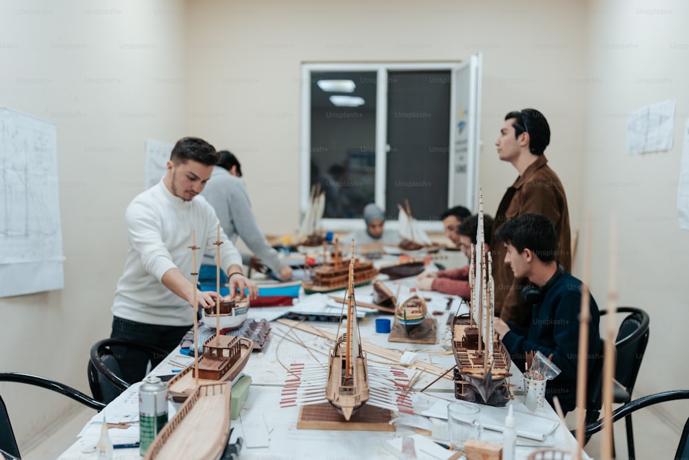 a group of people standing around a table with model ships on it