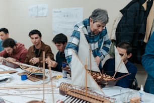 a group of men sitting around a table working on a model sailboat