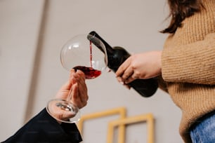 une femme versant un verre de vin rouge dans la main d’une autre femme