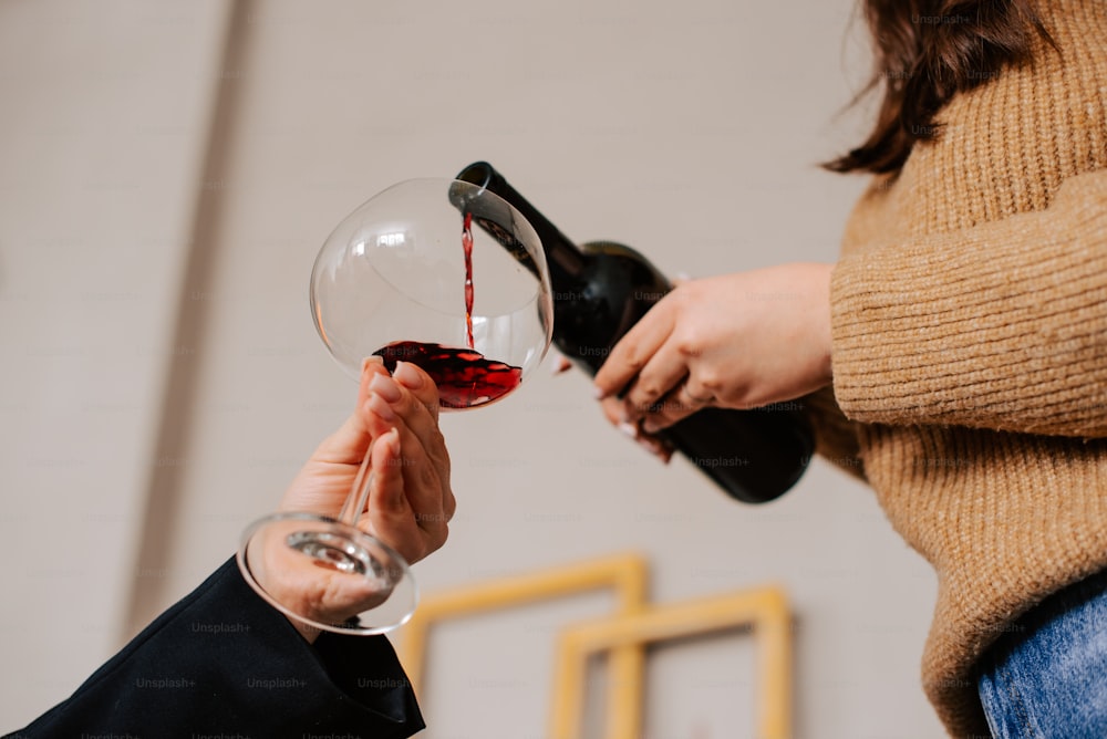 a woman pouring a glass of red wine into another woman's hand