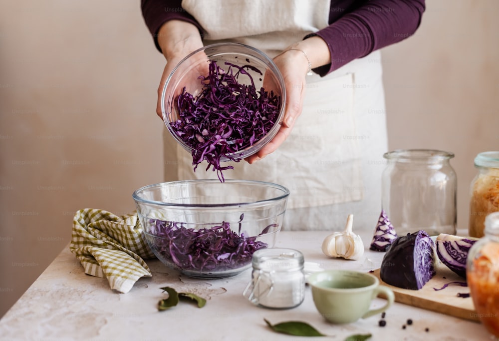a woman in an apron is adding purple cabbage to a bowl
