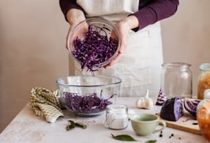a woman in an apron is adding purple cabbage to a bowl