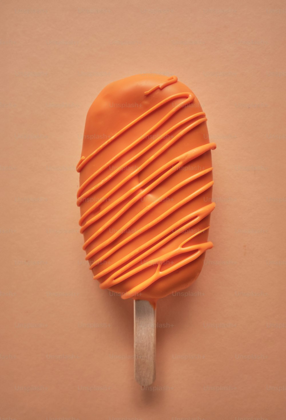 an orange lollypop on a stick on a pink background