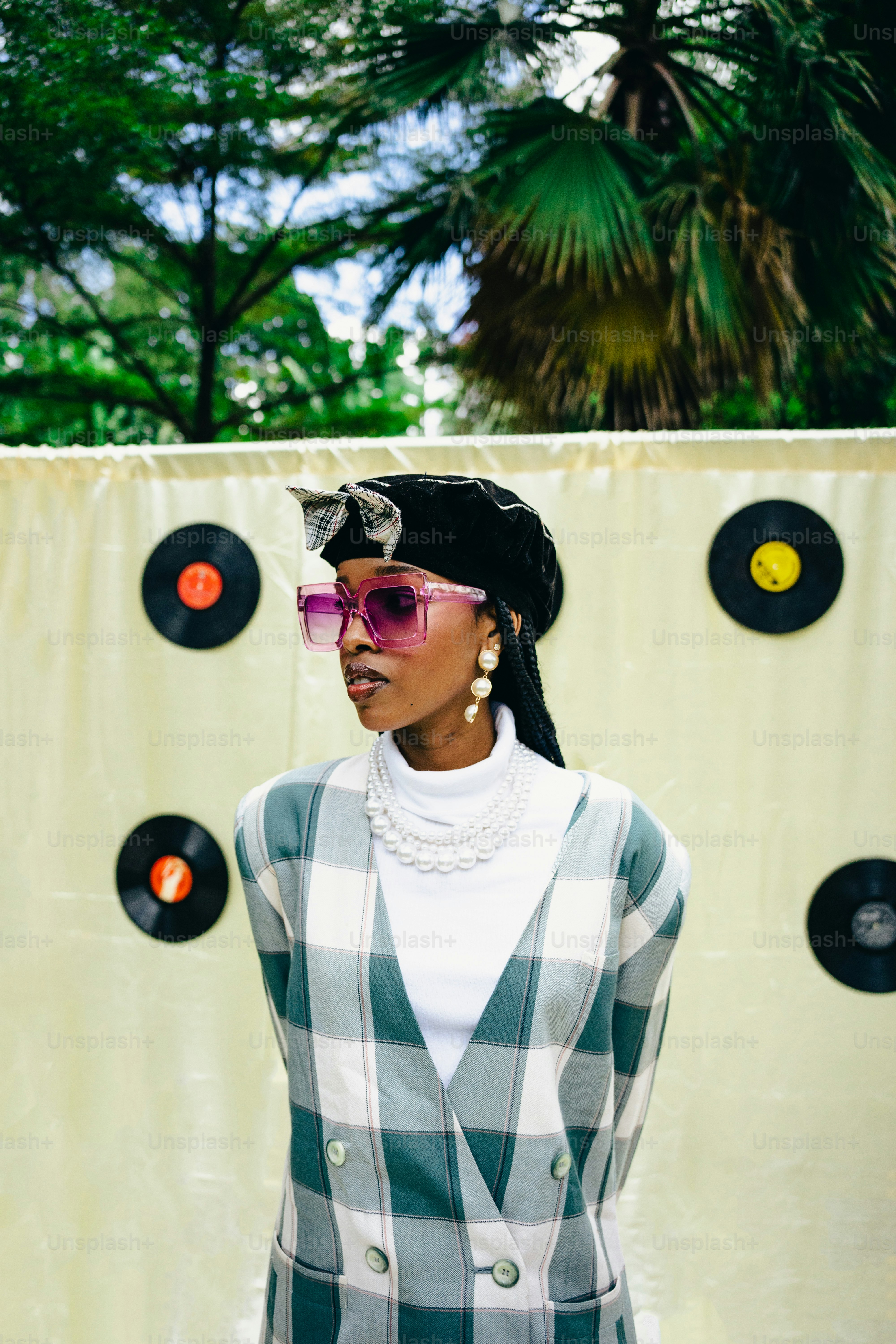a woman wearing a hat and sunglasses standing in front of a wall