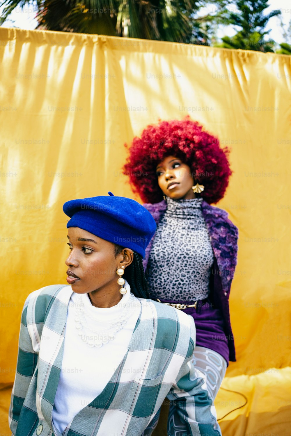 two women standing next to each other in front of a yellow wall