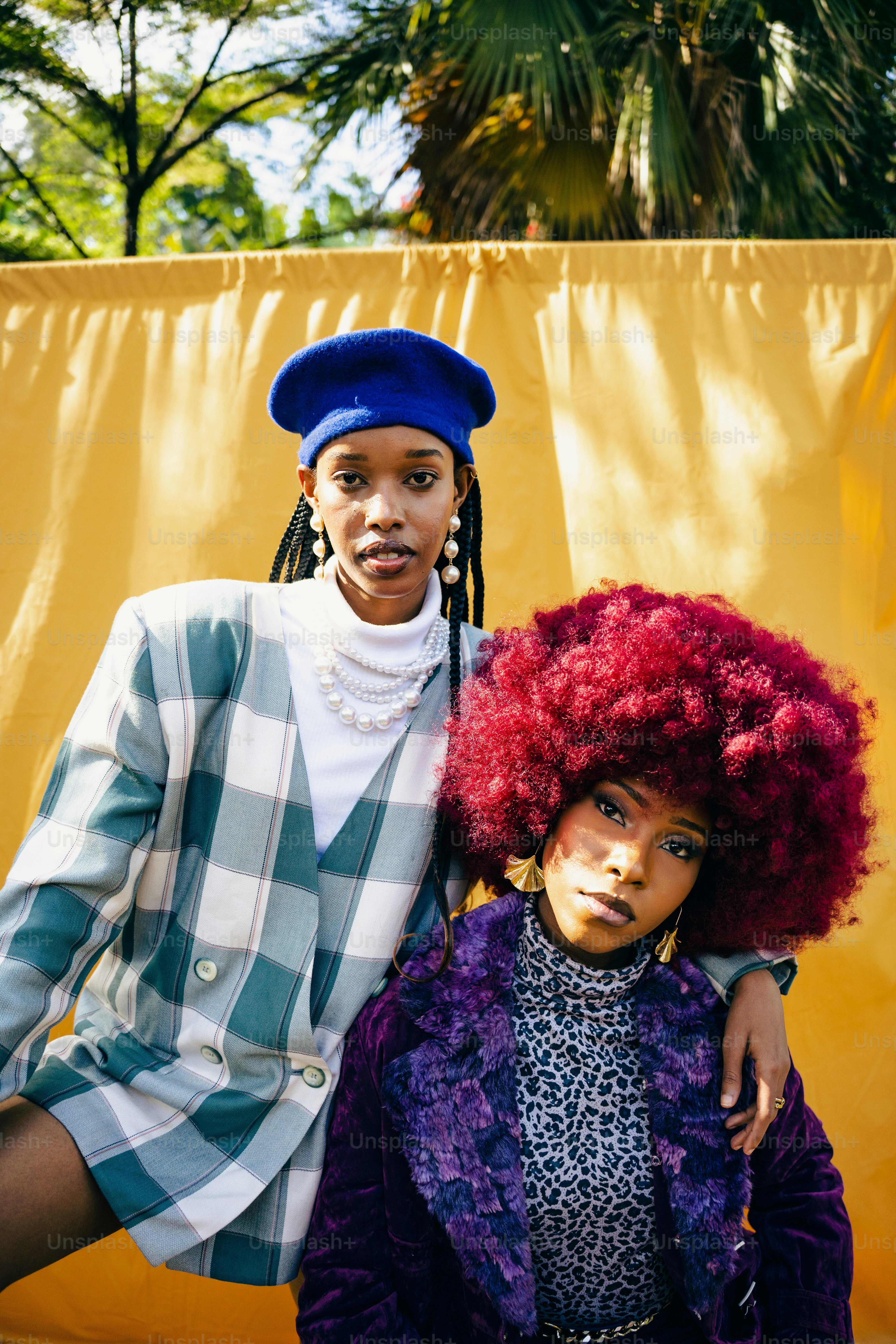 two women standing next to each other in front of a yellow wall