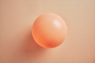 une boule orange sur une surface rose clair